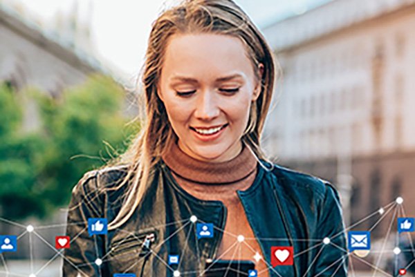 A woman in a leather jacket smiles while using her phone outside. Social media icons and connectivity lines overlay the image, conveying digital engagement.